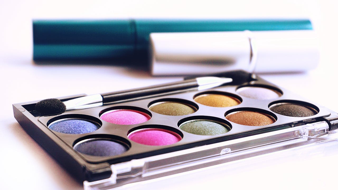 who-we-are Close-up of colorful eyeshadow palette with brush, ideal for fashion and beauty themes.