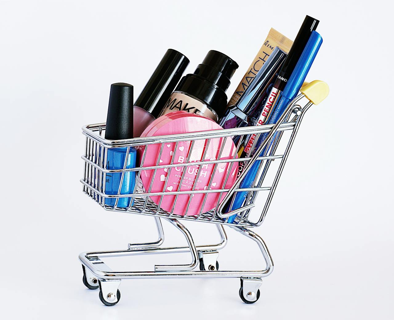 team-02 Miniature shopping cart filled with a variety of cosmetics on a white background.